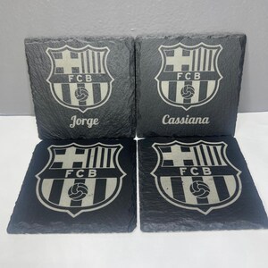 May include: Four black slate coasters with a white FC Barcelona logo and the names Jorge, Cassiana, and FCB.