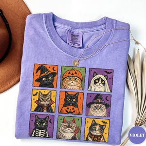 Może przedstawiać: Fioletowy t-shirt z krótkim rękawem z nadrukiem graficznym składającym się z dziewięciu kwadratowych paneli, z których każdy przedstawia innego kota w kostiumie na Halloween, w tym czarownice, dynie, duchy i szkielety, z metką Comfort Colors.