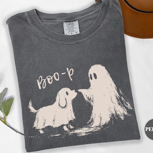 May include: A charcoal gray t-shirt featuring a cream-colored graphic of a dog and a ghost with the text "BOO-p". The shirt has a crew neckline and a Comfort Colors brand label at the inner collar, indicating a size large, with a pepper color label.