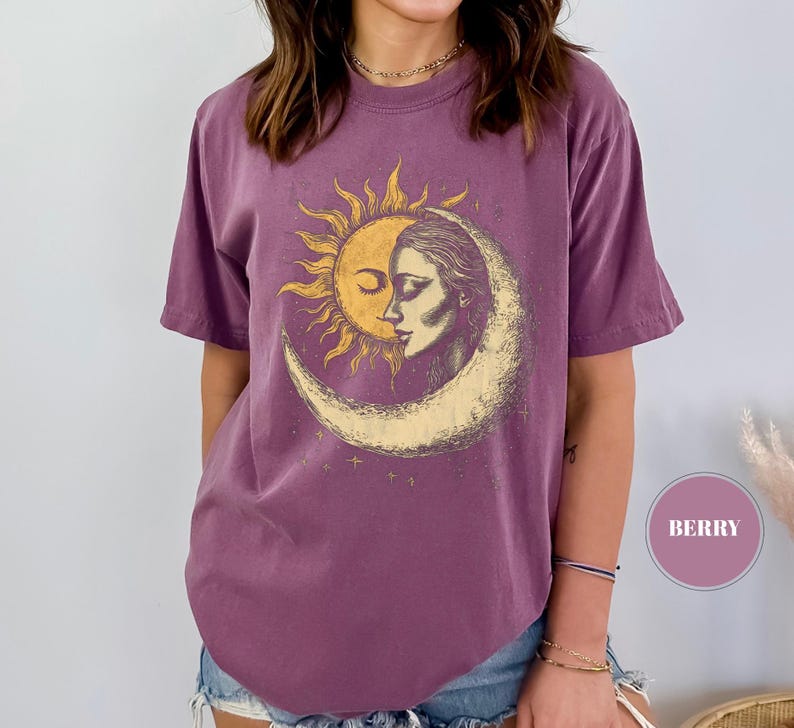 May include: Berry-colored t-shirt featuring a sun and moon graphic. The design depicts a sun with a face embracing a woman's face within a crescent moon. The shirt has short sleeves and a relaxed fit, perfect for casual wear.