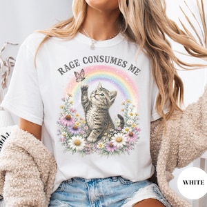 May include: White t-shirt with a graphic of a kitten reaching for a butterfly in front of a rainbow. The text "RAGE CONSUMES ME" is above the kitten. The kitten is surrounded by flowers.