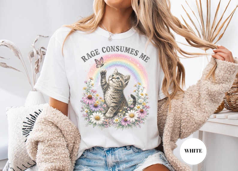 May include: White t-shirt with a graphic of a kitten reaching for a butterfly in front of a rainbow. The text "RAGE CONSUMES ME" is above the kitten. The kitten is surrounded by flowers.