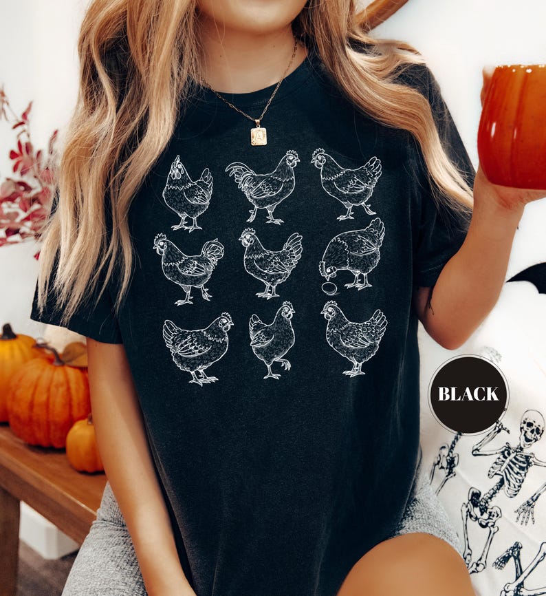 May include: Black t-shirt featuring a grid of nine white chicken illustrations. The shirt has a crew neck and short sleeves. A round sticker on the shirt says "BLACK". The shirt is worn by a person.