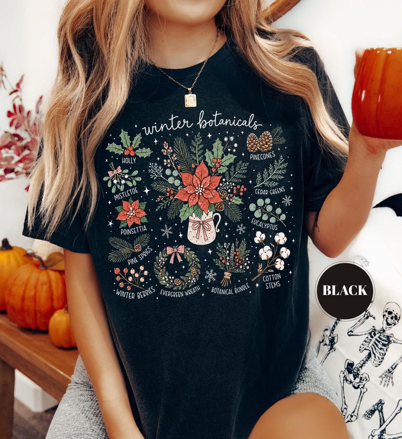 May include: A black t-shirt featuring a graphic print titled winter botanicals. The design displays various illustrations including holly, mistletoe, poinsettia, pinecones, cedar greens, eucalyptus, pine sprigs, winter berries, a wreath, and cotton stems.
