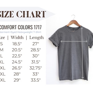 May include: A gray Comfort Colors 1717 garment-dyed heavyweight t-shirt hangs on a wooden hanger. The image includes a size chart with measurements in inches for sizes S through 4XL. The shirt's width ranges from 18.5" to 29", and the length from 27" to 33.5".