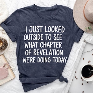 a dark blue t-shirt with white text, a hat, a cup of coffee, a book, and some other items arranged on a bed or a table.