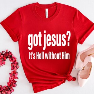 A red t-shirt with the text "got jesus? It's Hell without Him" printed on it, along with a pair of pink high heels and a heart-shaped arrangement of red flowers.