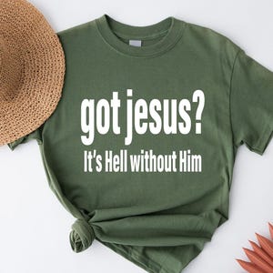 A green t-shirt with the text "got jesus? It's Hell without Him" printed on it, along with a straw hat and some red objects in the background.