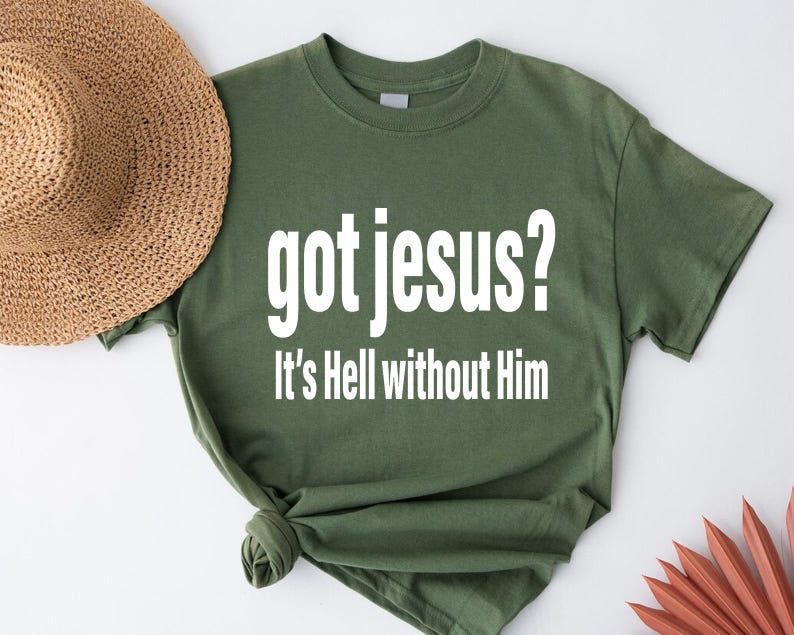 A green t-shirt with the text "got jesus? It's Hell without Him" printed on it, along with a straw hat and some red objects in the background.