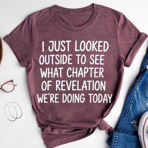 a purple t-shirt with white text, a pair of blue jeans, a pair of glasses, and a pair of white sneakers, all laid out on a white background.