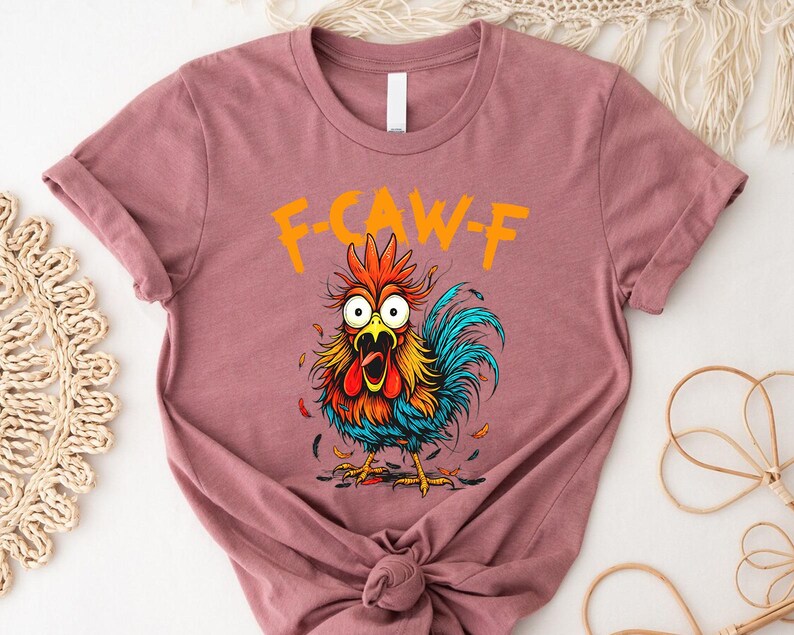 A pink t-shirt with a colorful illustration of a rooster and the text "F-CAWF-F" printed on it.