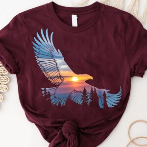 A burgundy t-shirt with a graphic design depicting an eagle in flight against a sunset landscape.