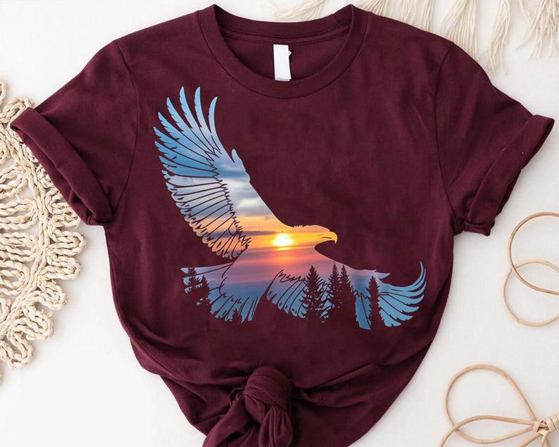 A burgundy t-shirt with a graphic design depicting an eagle in flight against a sunset landscape.