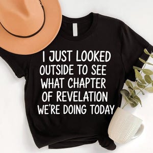 a black t-shirt with white text, a brown hat, a white mug, and a plant, all arranged on a white background.