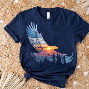 A navy blue t-shirt with a graphic design depicting a soaring eagle against a sunset landscape.