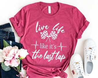 May include: A heathered dark pink short-sleeve t-shirt featuring white screen-printed text that reads "live life like it's the last lap" with two crossed checkered racing flags and a heartbeat line graphic centered on the front of the garment.