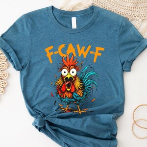 A blue t-shirt with a colorful cartoon rooster graphic and the text "F-CAWF" printed on it.