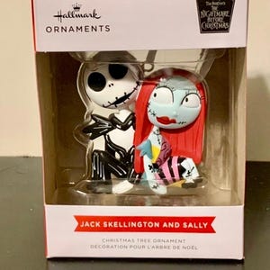 May include: A Hallmark Christmas tree ornament featuring Jack Skellington and Sally from "The Nightmare Before Christmas." The figures are in a clear plastic case, with a red and white box. The box reads "Jack Skellington and Sally" and "Christmas Tree Ornament."