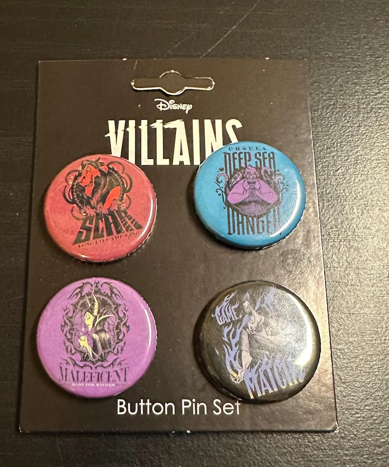 K&ouml;nnte beinhalten: Ein Disney Villains Button-Pin-Set. Das Set enth&auml;lt vier runde Pins mit Bildern von Disney-B&ouml;sewichten. Die Pins sind rot, blau, lila und schwarz. Der Text "Button Pin Set" befindet sich am unteren Rand der Karte.