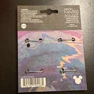 K&ouml;nnte beinhalten: Eine Packung mit vier Anstecknadeln mit Metallverschl&uuml;ssen. Die R&uuml;ckseite der Karte hat ein farbenfrohes abstraktes Design, das Neon Tuesday-Logo und das Disney-Branding. Die Karte enth&auml;lt auch eine Warnung vor Kleinteilen.