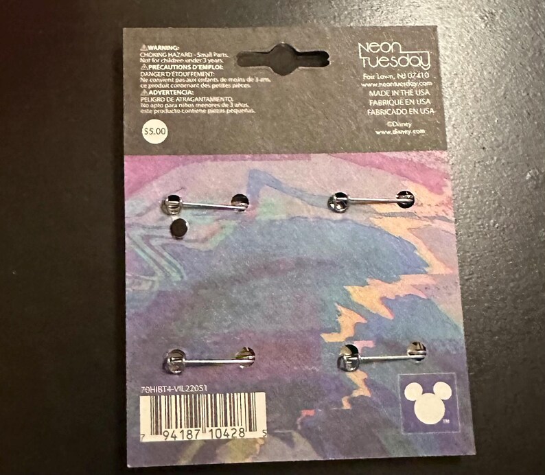 K&ouml;nnte beinhalten: Eine Packung mit vier Anstecknadeln mit Metallverschl&uuml;ssen. Die R&uuml;ckseite der Karte hat ein farbenfrohes abstraktes Design, das Neon Tuesday-Logo und das Disney-Branding. Die Karte enth&auml;lt auch eine Warnung vor Kleinteilen.