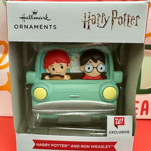 Może przedstawiać: Ozdoba choinkowa Hallmark z Harrym Potterem i Ronem Weasleyem w jasnozielonym samochodzie. Ozdoba ma żółte reflektory i tekst "Harry Potter" i "Ron Weasley".