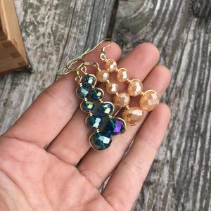 May include: A pair of dangle earrings with gold wire and faceted glass beads. One earring has peach-colored beads and the other has iridescent green beads.