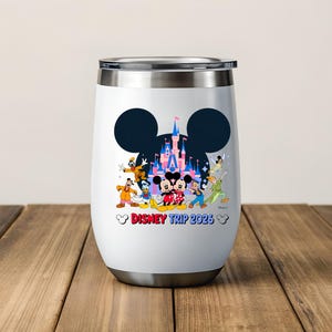 May include: White insulated tumbler with a silver rim and base. The tumbler features a black Mickey Mouse silhouette with a castle and Disney characters. The text "Disney Trip 2023" is printed in red and blue.