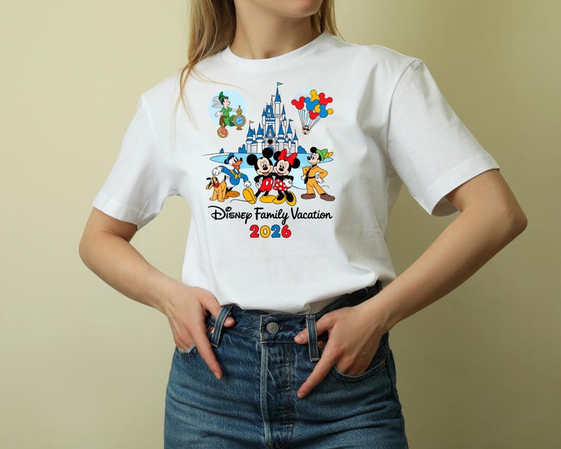 May include: White t-shirt featuring a colorful graphic of Disney characters, including Mickey and Minnie Mouse, Donald Duck, and Peter Pan, with a castle and balloons. The text "Disney Family Vacation 2026" is printed below the characters.