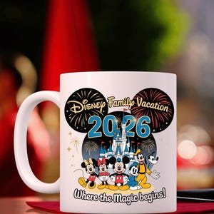 May include: White ceramic mug featuring a Disney Family Vacation design for 2026. The design includes Mickey and Minnie Mouse, Donald Duck, Goofy, and a castle illustration. The text "Where the magic begins!" is also included.