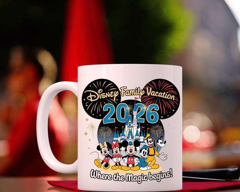 May include: White ceramic mug featuring a Disney Family Vacation design for 2026. The design includes Mickey and Minnie Mouse, Donald Duck, Goofy, and a castle illustration. The text "Where the magic begins!" is also included.