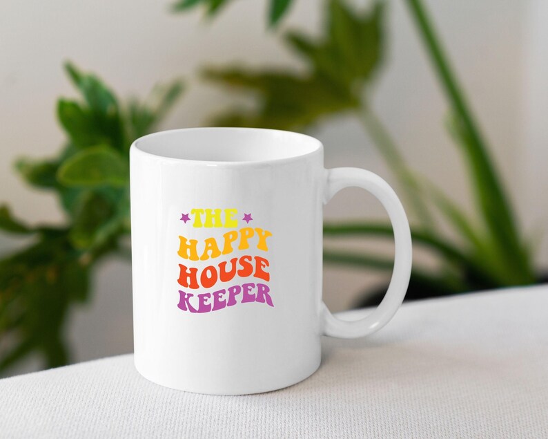 May include: White ceramic mug with a colourful graphic that reads "The Happy House Keeper" in a retro font.
