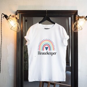 May include: White t-shirt with a rainbow and heart graphic and the text "Housekeeper".