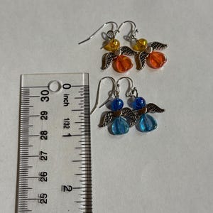 Pu&ograve; includere: Due paia di orecchini a forma di angelo fatti a mano. Un paio presenta perline arancioni e gialle, mentre l'altro ha perline blu. Ogni orecchino ha ali e ganci per le orecchie in metallo color argento. Gli orecchini sono lunghi circa 2,5 cm.