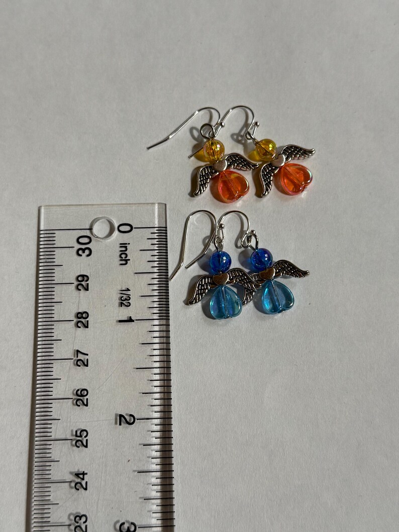 Pu&ograve; includere: Due paia di orecchini a forma di angelo fatti a mano. Un paio presenta perline arancioni e gialle, mentre l'altro ha perline blu. Ogni orecchino ha ali e ganci per le orecchie in metallo color argento. Gli orecchini sono lunghi circa 2,5 cm.