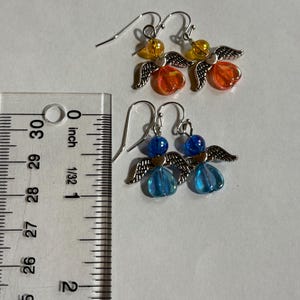 Pu&ograve; includere: Due paia di orecchini a forma di angelo fatti a mano. Un paio presenta perline arancioni e gialle, mentre l'altro ha perline blu. Ogni orecchino ha ali color argento e un gancio per orecchie forate. Gli orecchini misurano circa 2.5 cm di lunghezza.