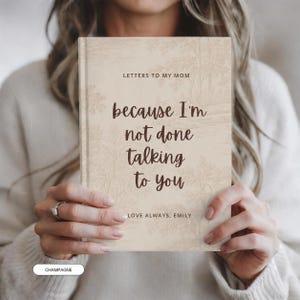 May include: A hardcover book with a light beige cover featuring a faint, monochromatic landscape illustration. The text reads: LETTERS TO MY MOM, because I'm not done talking to you, LOVE ALWAYS, EMILY. The lettering is in a dark brown, cursive font.