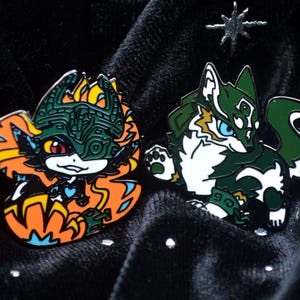 May include: Two enamel pins featuring stylized wolf-like creatures. One pin has orange, yellow, and black colors, while the other has green, white, and blue colors. Both pins are set against a black velvet background with star-shaped accents.
