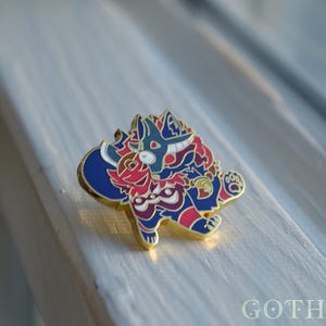 May include: A colorful enamel pin featuring a stylized creature with a blue and red color scheme, accented with gold. The pin has a detailed design and is set against a light background. The pin is a collectible item.
