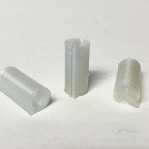 May include: Three small, cylindrical, off-white plastic components. Two are solid, while the third has a vertical slit. The objects are arranged on a white surface, suggesting a product or part.