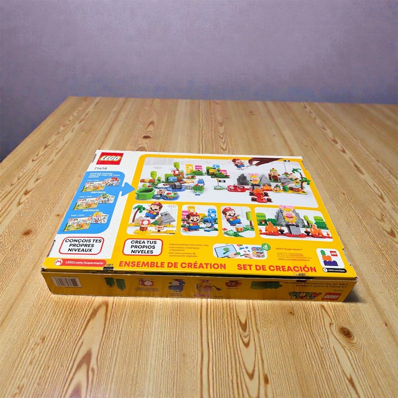 May include: A yellow LEGO Super Mario set box, featuring images of Mario characters and level designs. The box has text in multiple languages, including "CON&Ccedil;OIS TES PROPRES NIVEAUX" and "ENSEMBLE DE CR&Eacute;ATION". The box is on a wooden surface.