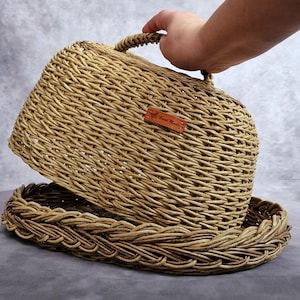 Op de afbeelding: Een geweven rieten mand met een deksel en een leren label met de tekst "Hand Made".