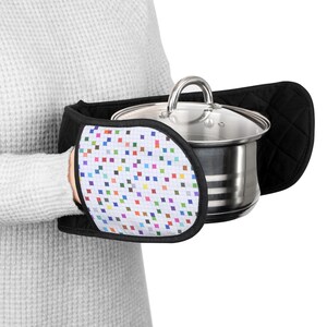 May include: A black and white pot holder with a colorful geometric pattern. The pot holder is designed to protect hands from heat while holding a hot pot or pan.