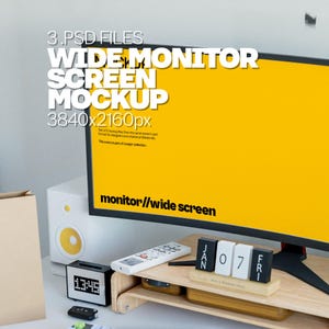 May include: A wide monitor screen mockup with a bright yellow display. The screen displays the text "WIDE MONITOR SCREEN MOCKUP 3840x2160px". A wooden desk organizer holds a calendar, remote, and other accessories. A speaker and clock are also visible.