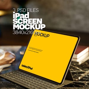 May include: A black iPad mockup with a yellow screen and a keyboard attached. The screen displays the text "tablet/iPad". The iPad is on a black marble surface with a stack of books in the background.