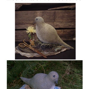 Puede incluir: Una paloma mamá de fieltro gris con un nido de paja y tres huevos blancos. La paloma está sentada en un libro azul con un patrón floral. El libro está en un lecho de agujas de pino verdes.