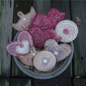 Könnte beinhalten: Eine Sammlung handgefertigter Filz-Ornamente in Form von Herzen, Vögeln und einem Lebkuchenmann. Die Ornamente sind mit weißer und roter Farbe verziert und haben einen verschneiten, winterlichen Look.