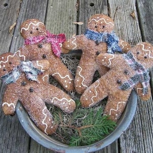 May include: Four gingerbread men with white icing and sprinkles, wearing scarves. The gingerbread men are arranged in a metal bowl with green pine sprigs.