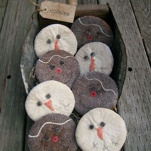 Könnte beinhalten: Eine Schaufel gefüllt mit acht selbstgemachten Schneemann-Keksen. Die Kekse sind weiß und braun mit schwarzen Augen, orangenen Nasen und roten Mündern. Die Kekse sind mit weißem Zuckerguss und Streuseln verziert. Die Schaufel ist aus Metall und hat einen Holzgriff. Ein braunes Papieretikett mit dem Wort "COOKIES" ist am Griff befestigt.