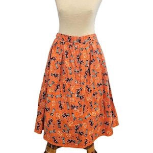 May include: Orange button-down skirt with a black cat print. The skirt features a repeating pattern of black cats playing musical instruments and the word "Pete" in white. The skirt is knee-length and has a button closure.